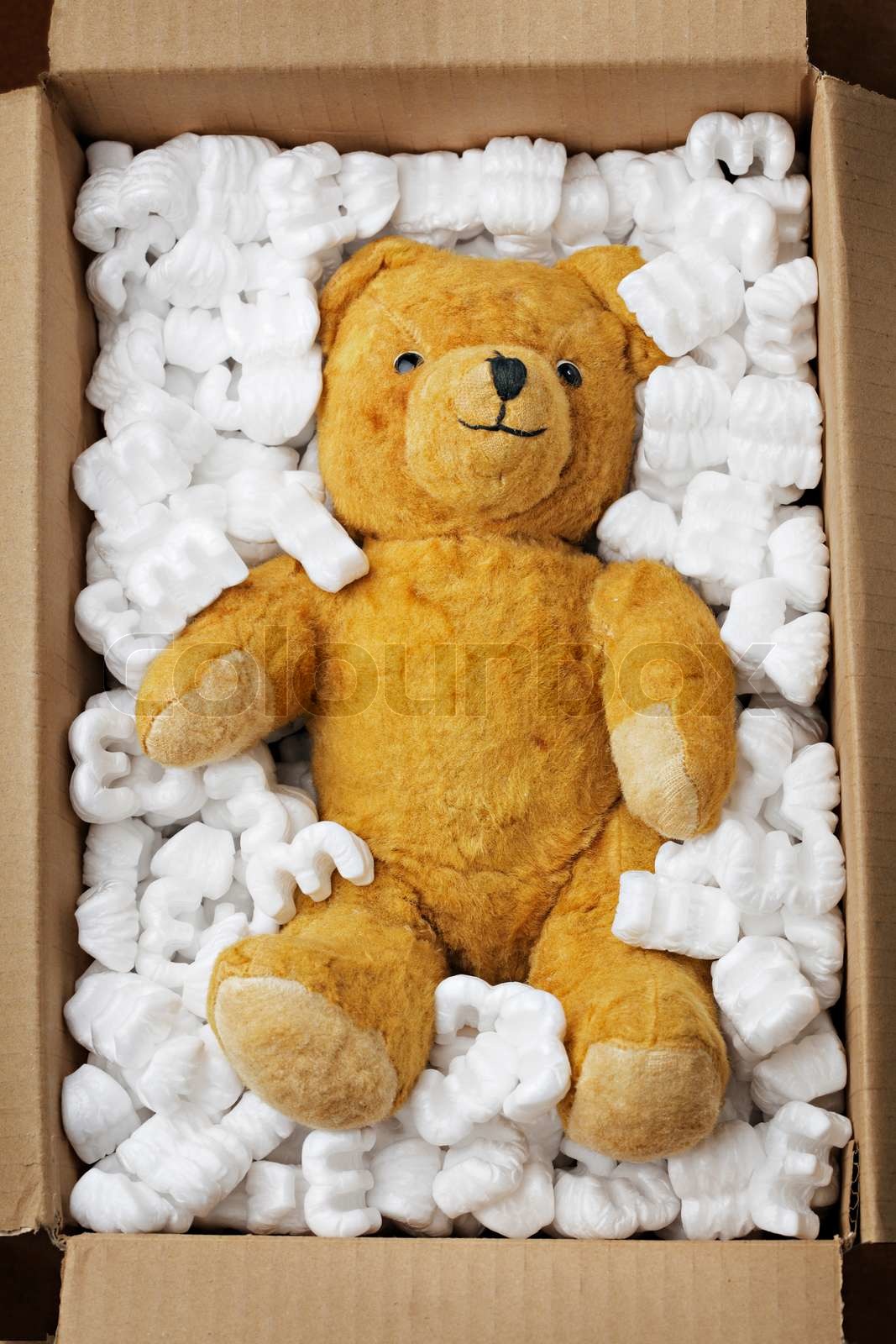 Old teddy bear in a cardboard box with styrofoam packaging Colourbox