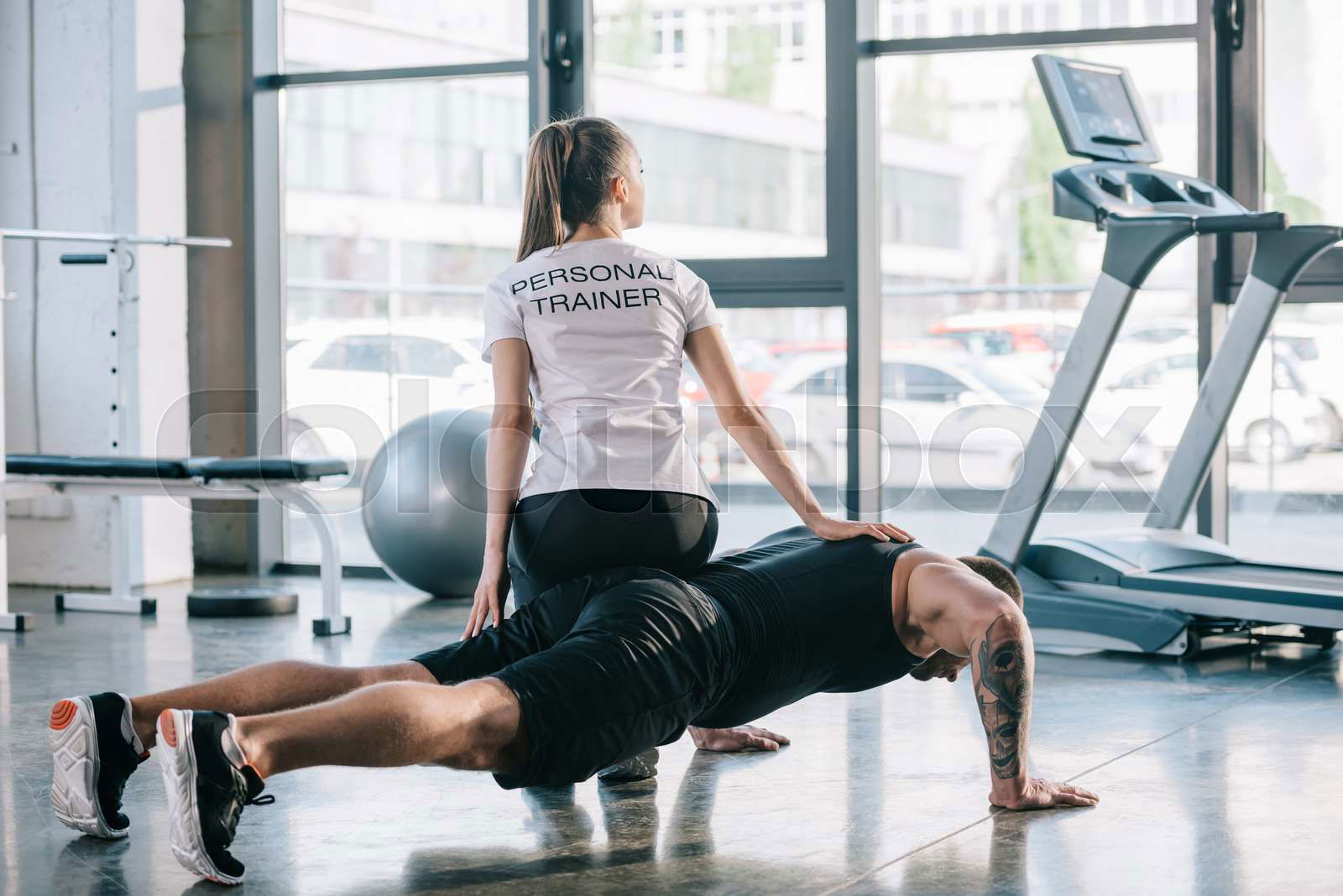 Sportsman doing push ups with female personal trainer sittin Colourbox