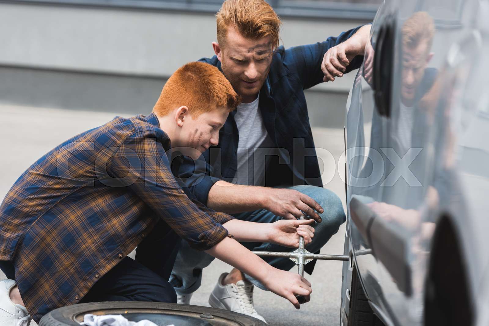 Side view of father and son changing tire in car with wheel wrench