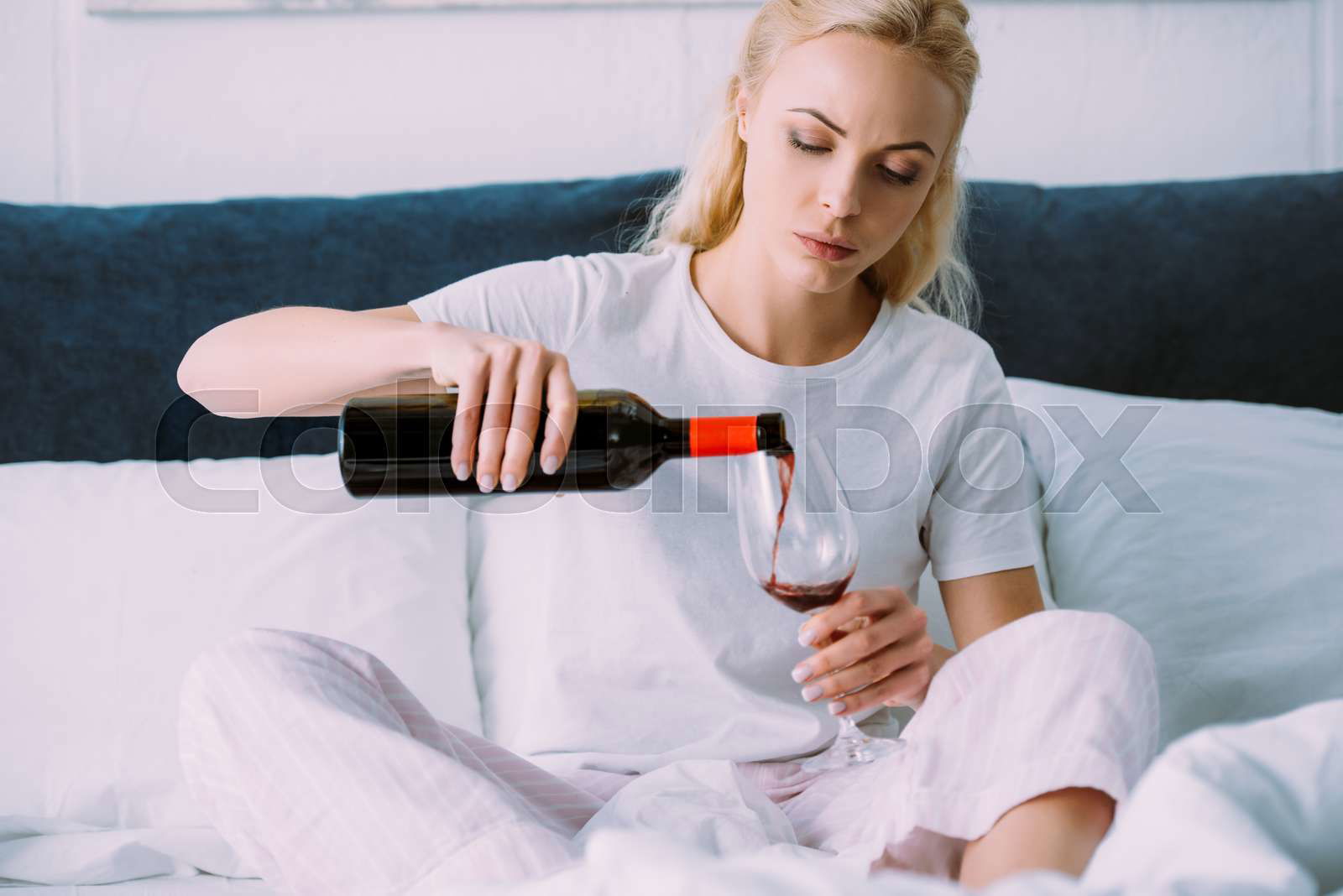 sad woman in pajamas pouring red wine in bed at home Stock image