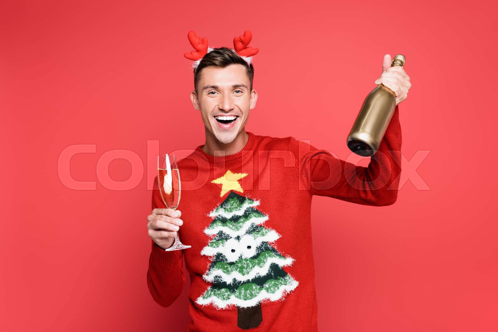 Cheerful man in christmas sweater and headband holding bottle and