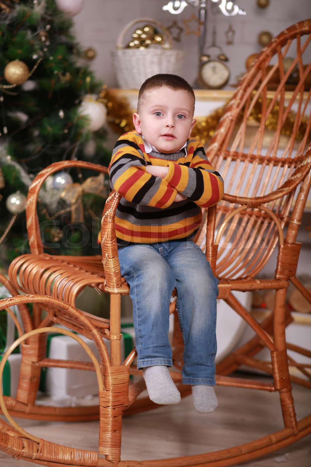 Cute little boy sitting in rocking chair near christmas tree Colourbox