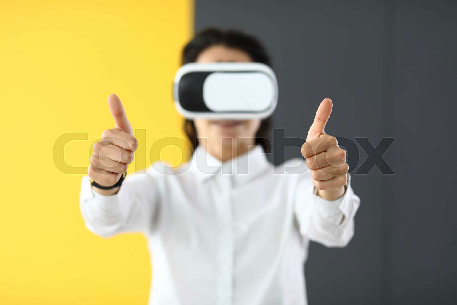Woman in virtual reality glasses stands and holds thumbs up. Colourbox