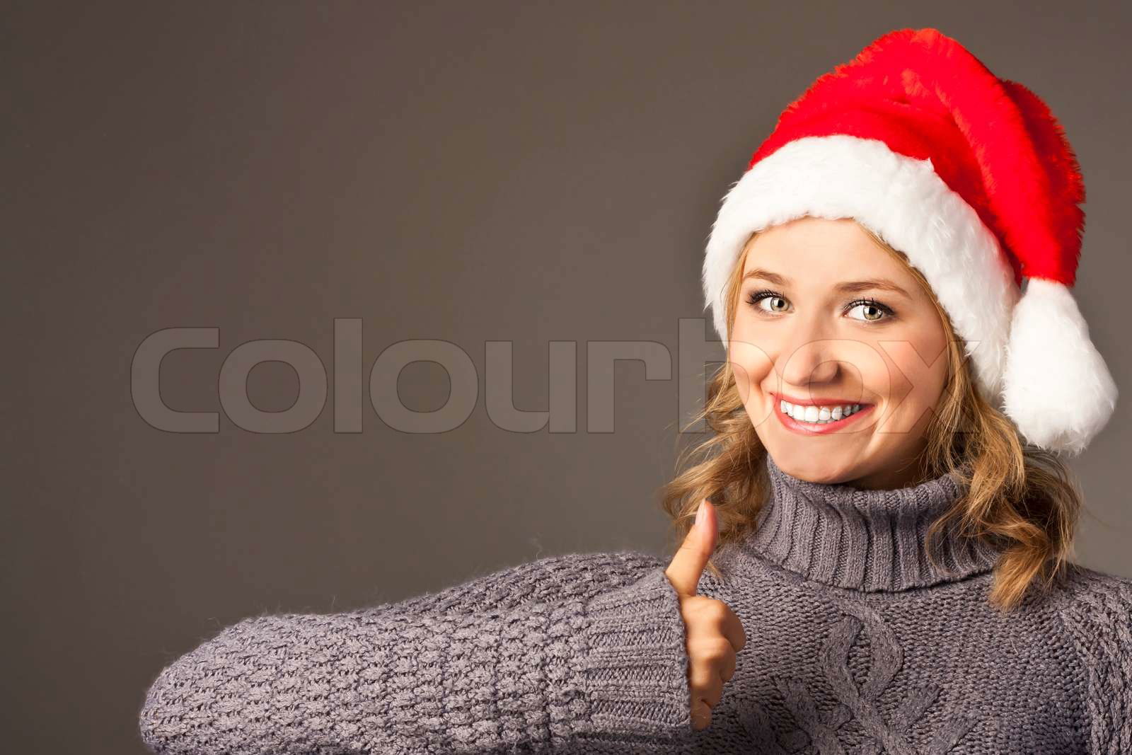 Happy smiley girl in santa hat showing thumbs up Colourbox