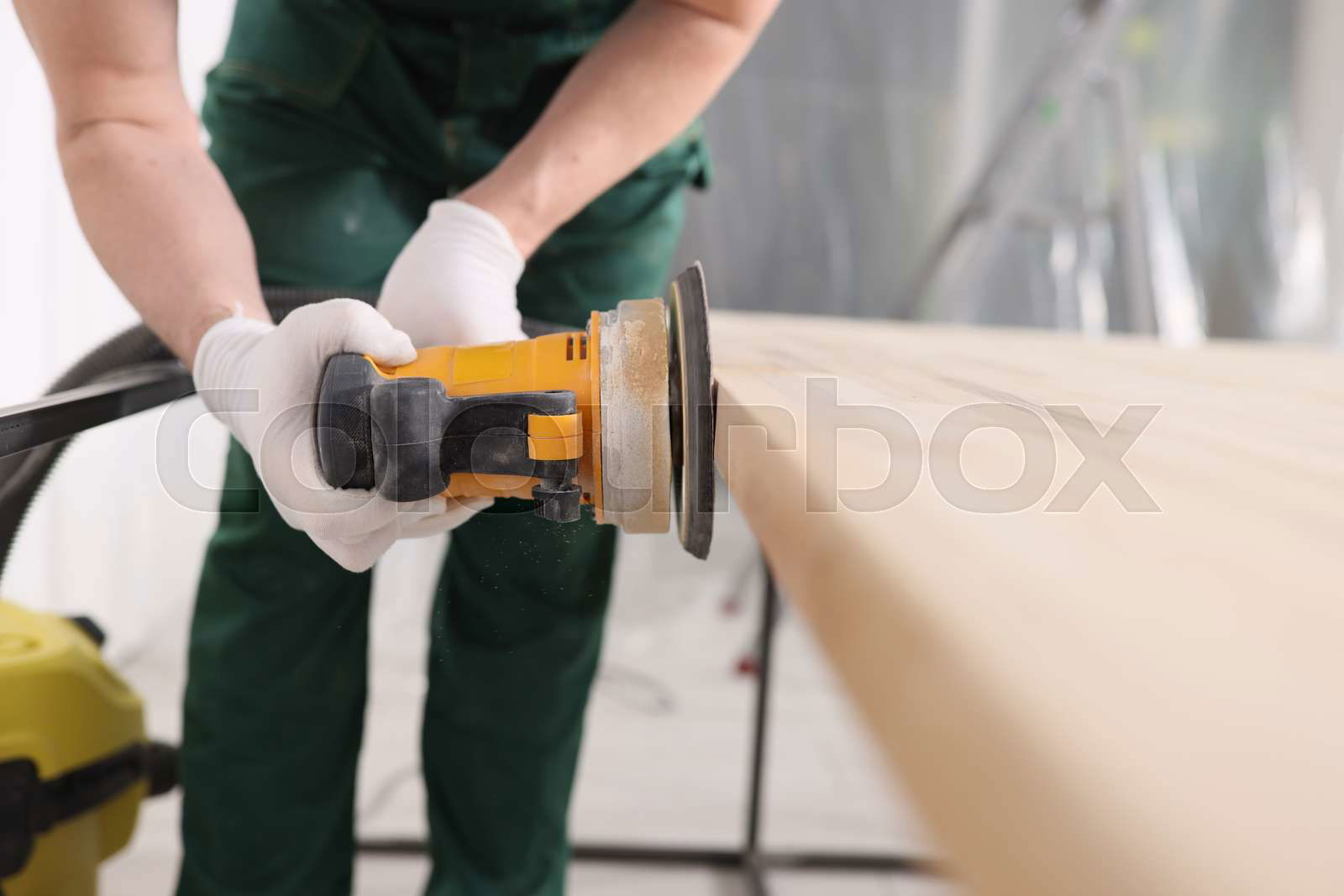 Carpenter in gloves processes wooden surface of table with g Colourbox