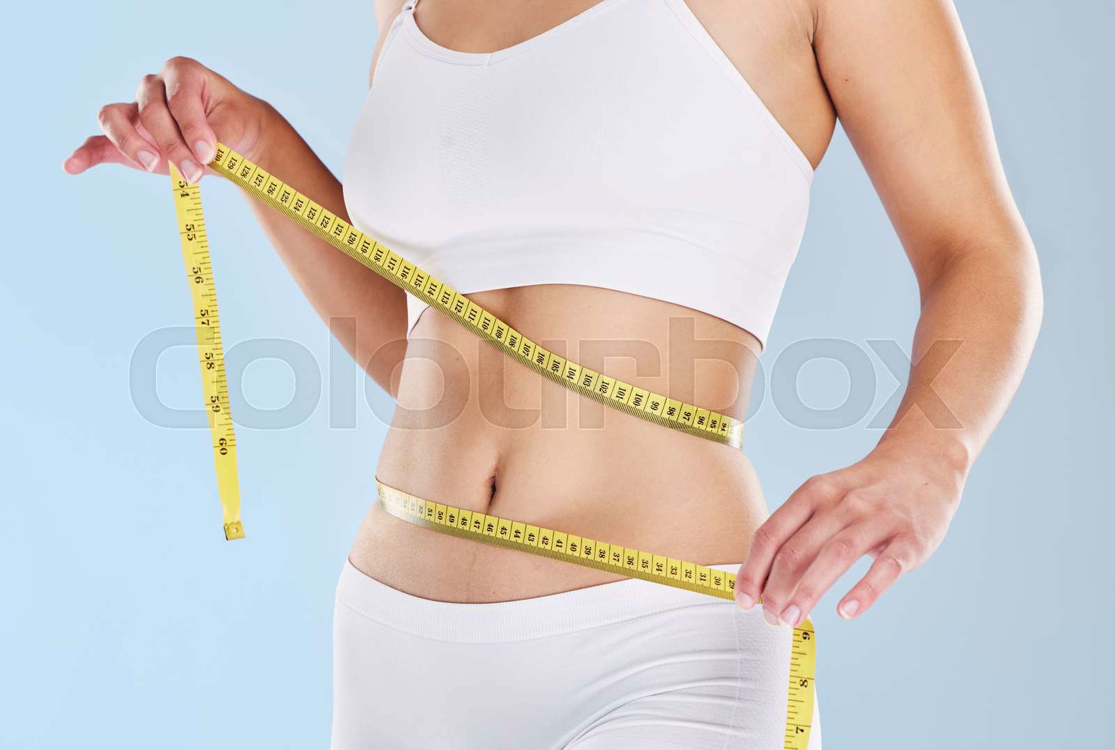 A woman using a measuring tape to measure her flat stomach a Colourbox