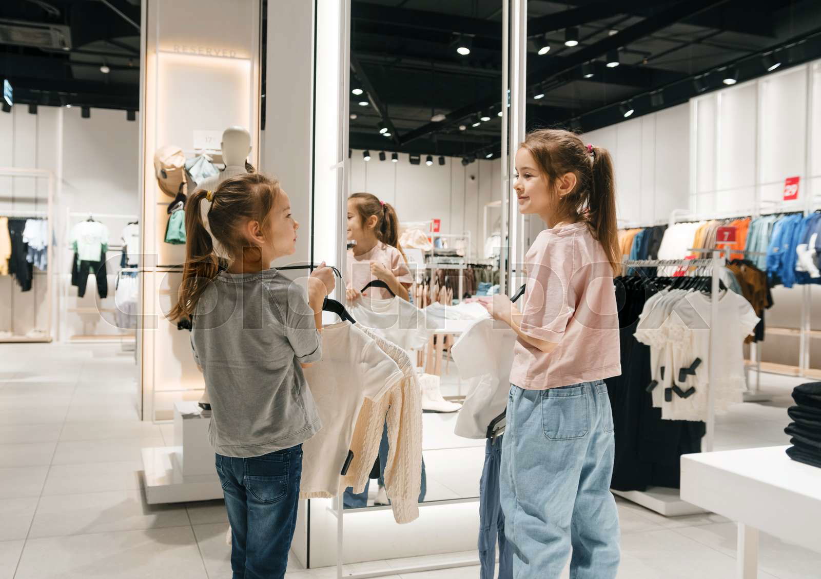 Two girls visibly excited browse through racks of clothing Colourbox